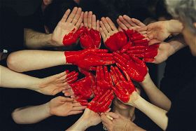 Viele Handflächen, in die ein großes, rotes Herz gemalt sind.